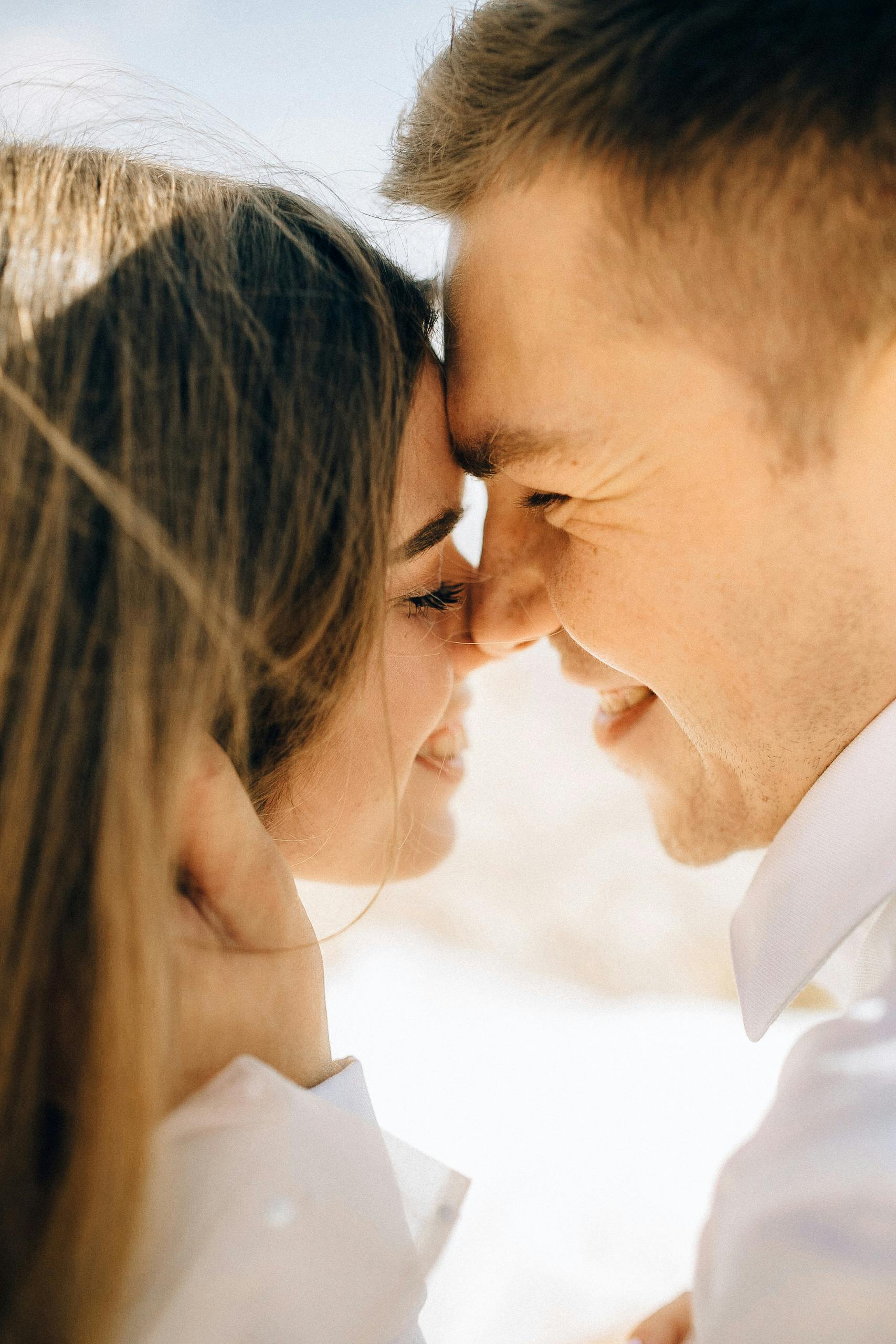 Close-up of a smiling couple standing forehead to forehead in soft natural light.